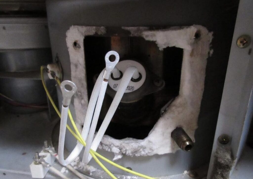 耐熱材で囲われたストーブ内部の点火ヒーター取り付け部。白い耐熱被覆の配線と丸端子が接続され、周囲には断熱材と金属フレームが見える。