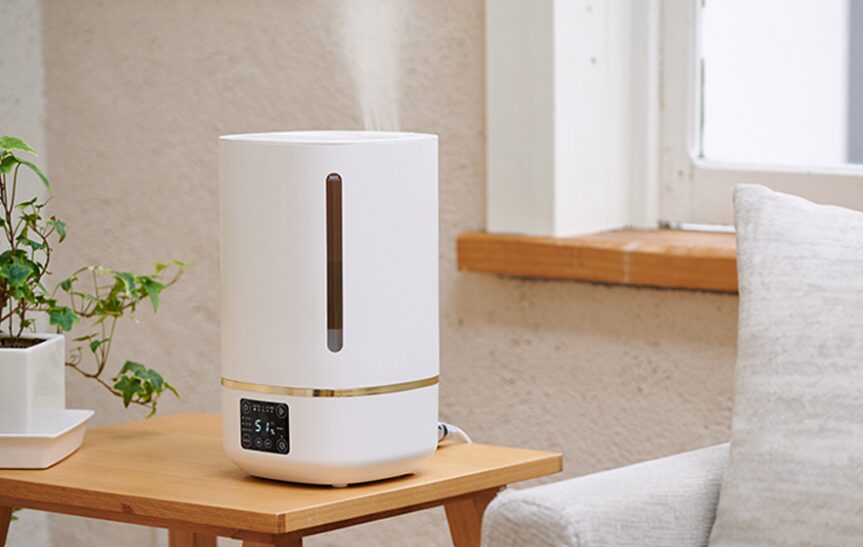 木製テーブルの上に設置された白色の据え置き型加湿器から、上方向へ細かな加湿ミストが噴き出している室内設置の様子。