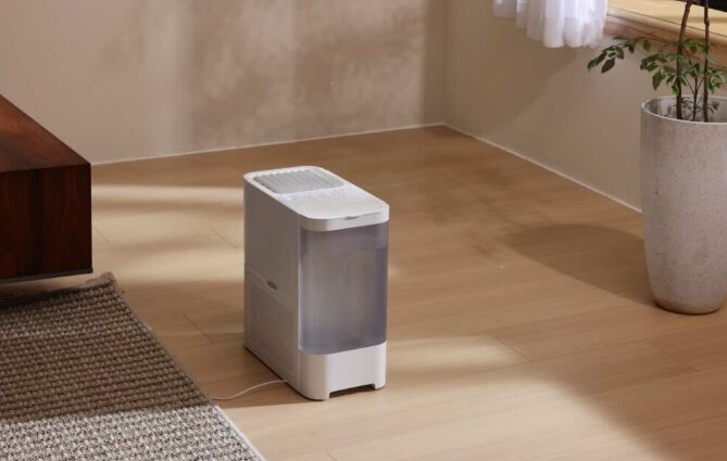 フローリングの床に設置されたコンパクトな加湿器が、窓からの自然光が入る室内で稼働している様子。