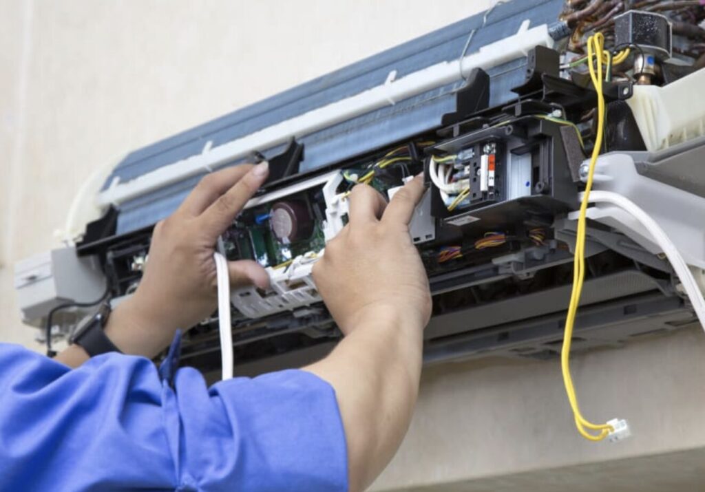 カバーを外したダイキン製エアコン室内機の内部で、技術者が基板や配線部分を点検・作業している様子。