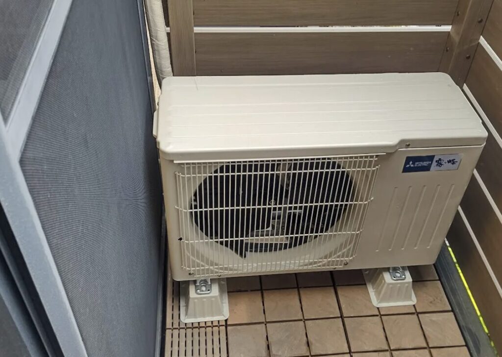 奥行きの限られたベランダに設置されたエアコン室外機。手すりや壁との距離が近い設置環境が分かる。