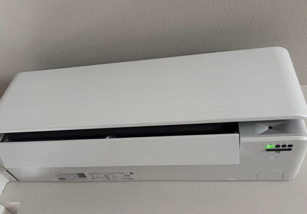 壁上部に設置された薄型エアコンの室内機。フラットな前面パネルと下部の吹き出し口が確認できる。