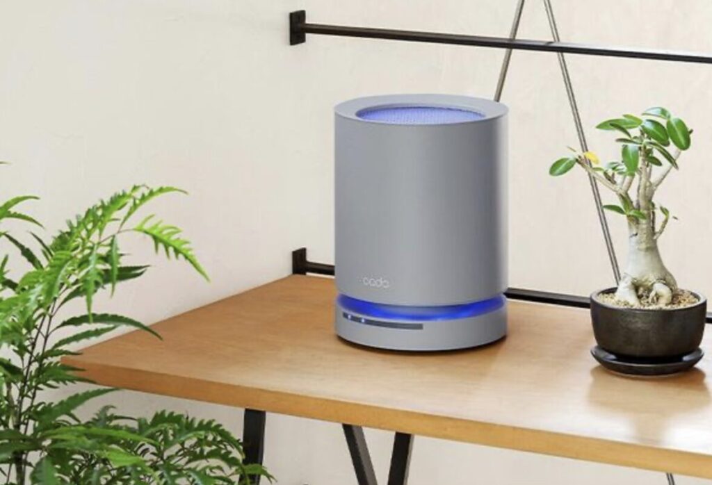 デスク上に設置された円筒形の卓上空気清浄機。青色の動作ランプが点灯し、観葉植物のある作業スペースに置かれている。