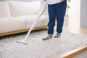 リビングのラグを、スティック型掃除機で掃除している使用シーン。