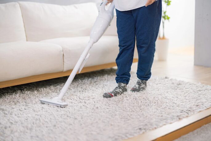 リビングのラグを、スティック型掃除機で掃除している使用シーン。
