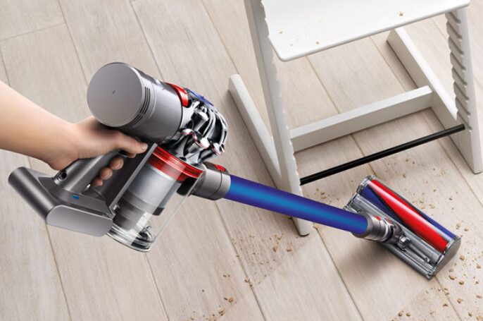 床に散らばったゴミを、フロアヘッド付きのダイソン製のコードレス掃除機で掃除している場面。