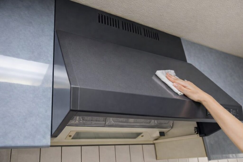 壁付けレンジフードの外装カバーを布で拭き掃除している手元の写真。黒い本体表面をやわらかい布で清掃している場面。