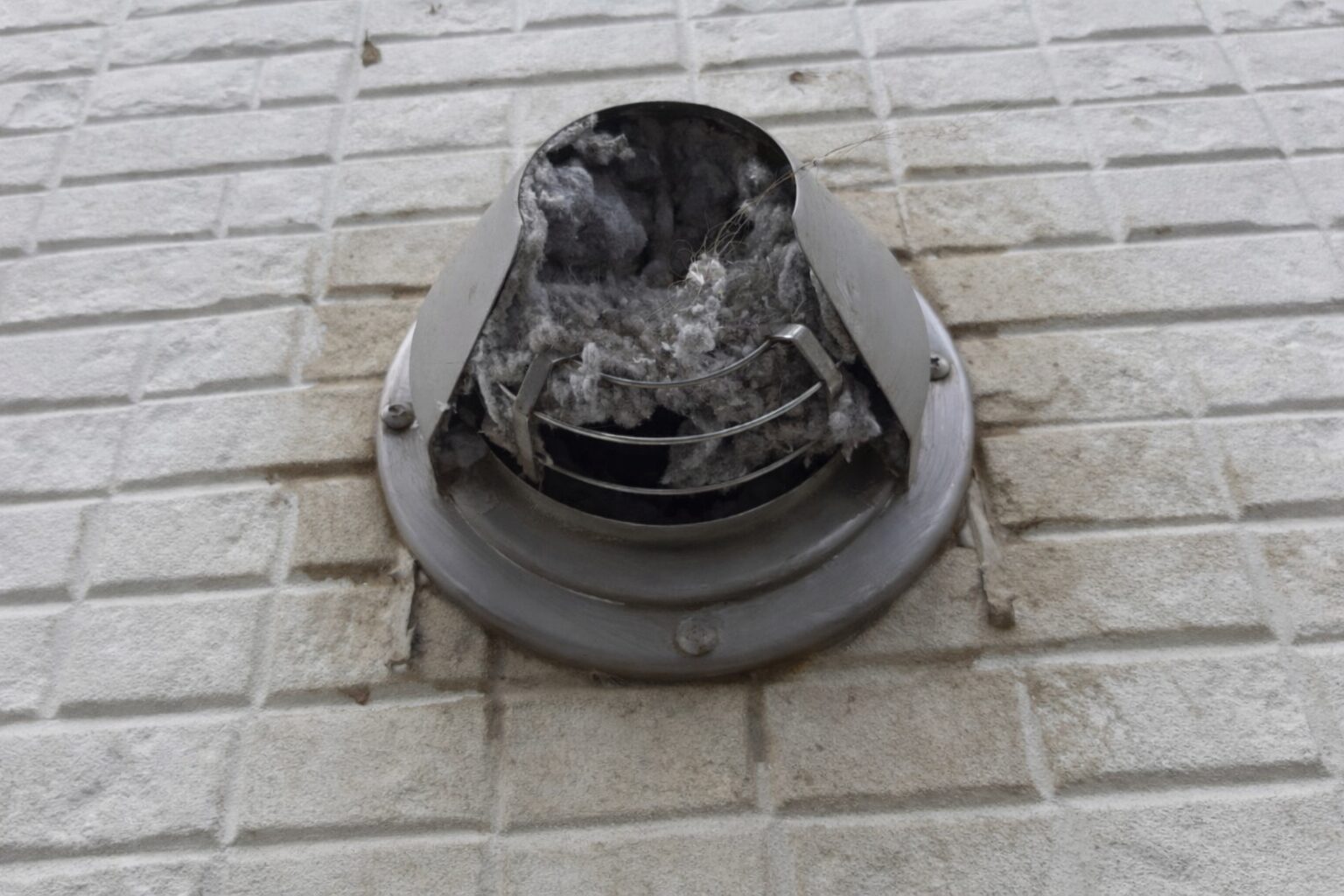 外壁の丸型排気口にホコリが詰まっている様子。乾太くんの排湿不良を示す詰まり事例。