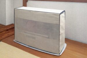 和室の畳とフローリングの境目に設置された石油ファンヒーターに、ベージュ色の専用カバーをかけて保管している様子。