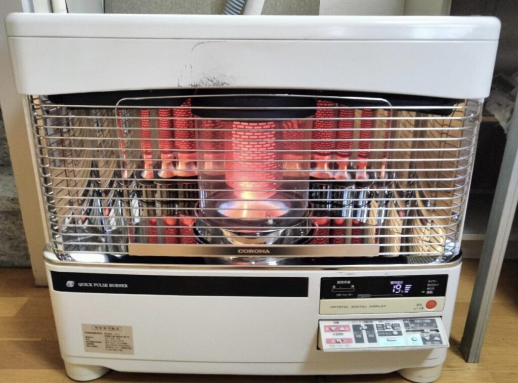 室内で燃焼中のコロナ製石油ストーブ。前面ガード越しに赤く発光する燃焼部と、右側のデジタル操作パネルが確認できる。