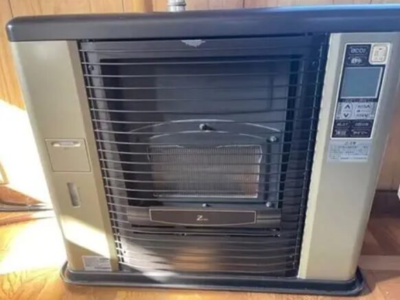 室内に設置されたサンポット製石油ストーブ。前面ガード越しに燃焼部が見え、右側に操作パネルを備えた据置型ストーブの外観が確認できる。