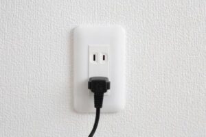 白い壁のコンセントに電源プラグが差し込まれ、コードが下方向に伸びている状態