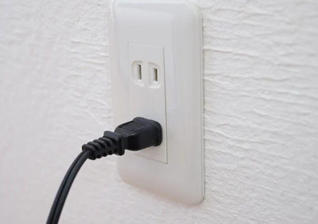壁のコンセントに黒い電源プラグが差し込まれている様子を近距離で撮影した写真