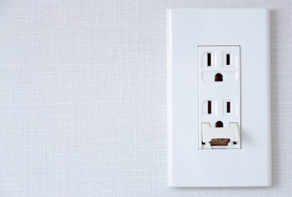 壁に設置されたアース付きコンセントで、下部のカバーが開いた状態