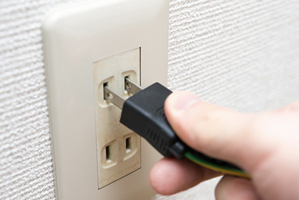 壁のコンセントに電源プラグを差し込もうとしている手元の様子