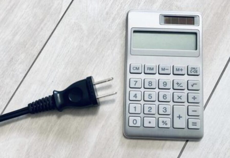 床の上に置かれた電源プラグと電卓が並び、電気代計算を連想させる構図