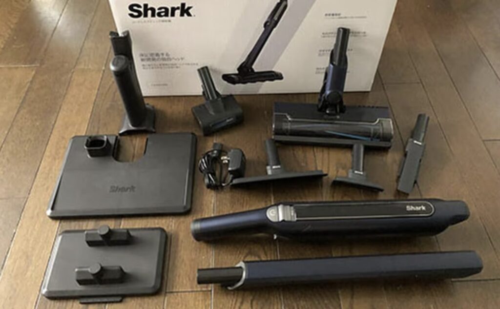 Shark製コードレス掃除機の本体と充電ドック、各種アタッチメントが床に並べられている様子