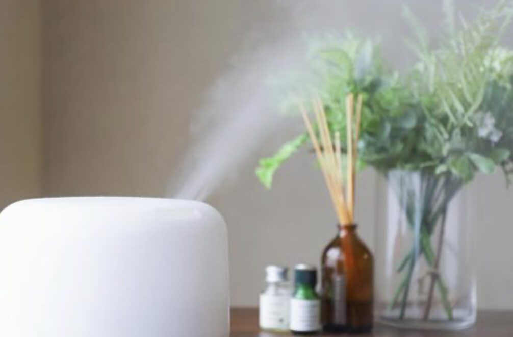 白い卓上加湿器からミストが立ち上り、背後にアロマボトルや観葉植物が置かれた室内の様子