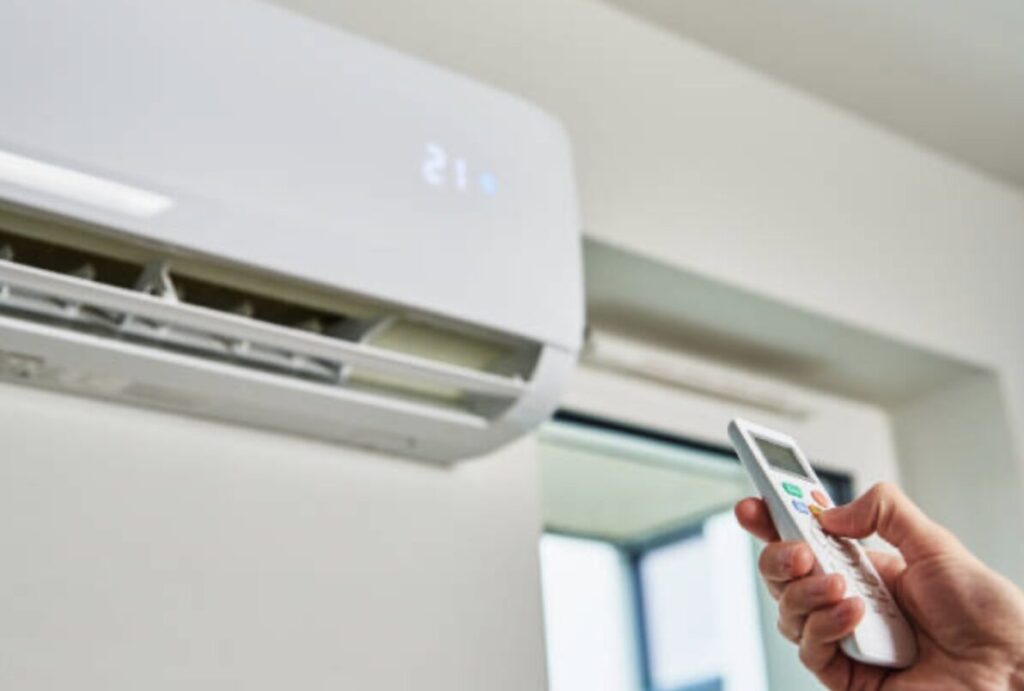 壁掛けエアコンに向けてリモコンを操作し、設定温度21度で運転している様子