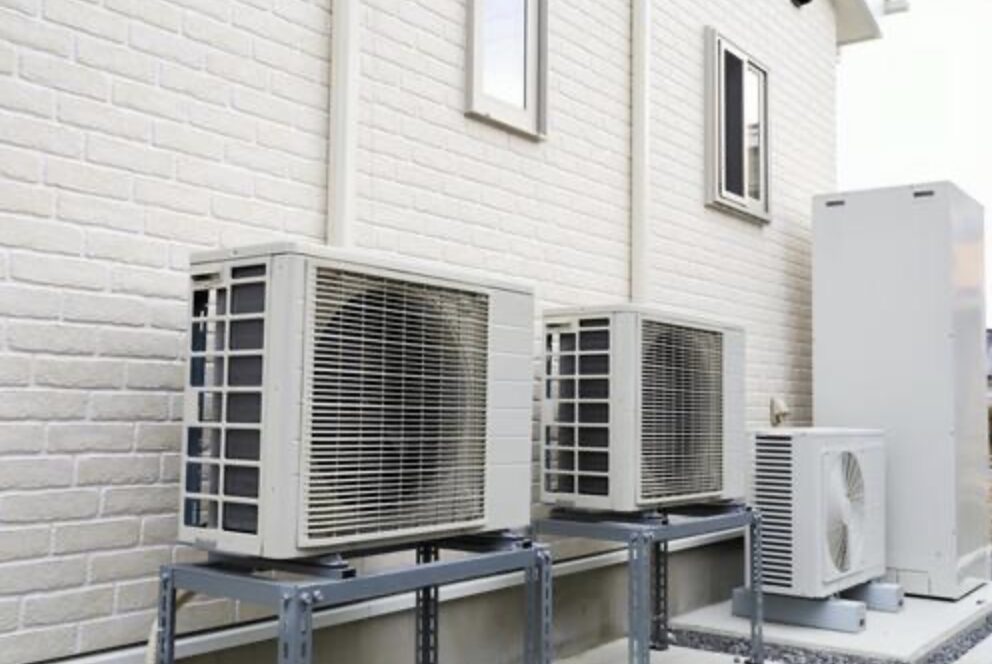 住宅外壁沿いに複数台のエアコン室外機と給湯設備が並んで設置されている様子