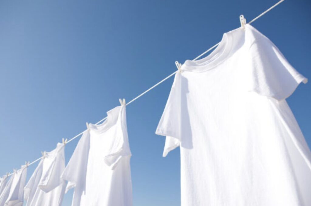 青空の下で外干しされた白いTシャツ。PM2.5や黄砂の影響が気になる洗濯物のイメージ。