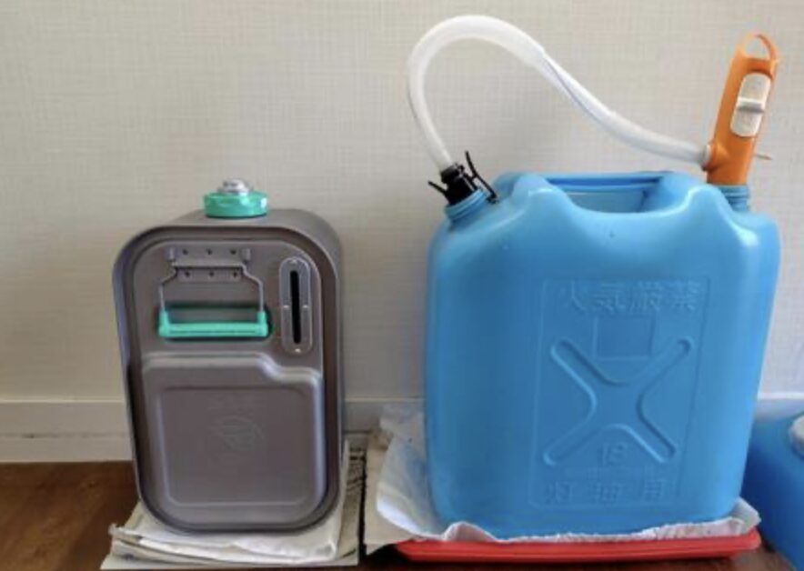 青い18L灯油ポリタンクに手動ポンプを差し込み、隣に金属製の灯油缶が並べて置かれている室内保管の様子。