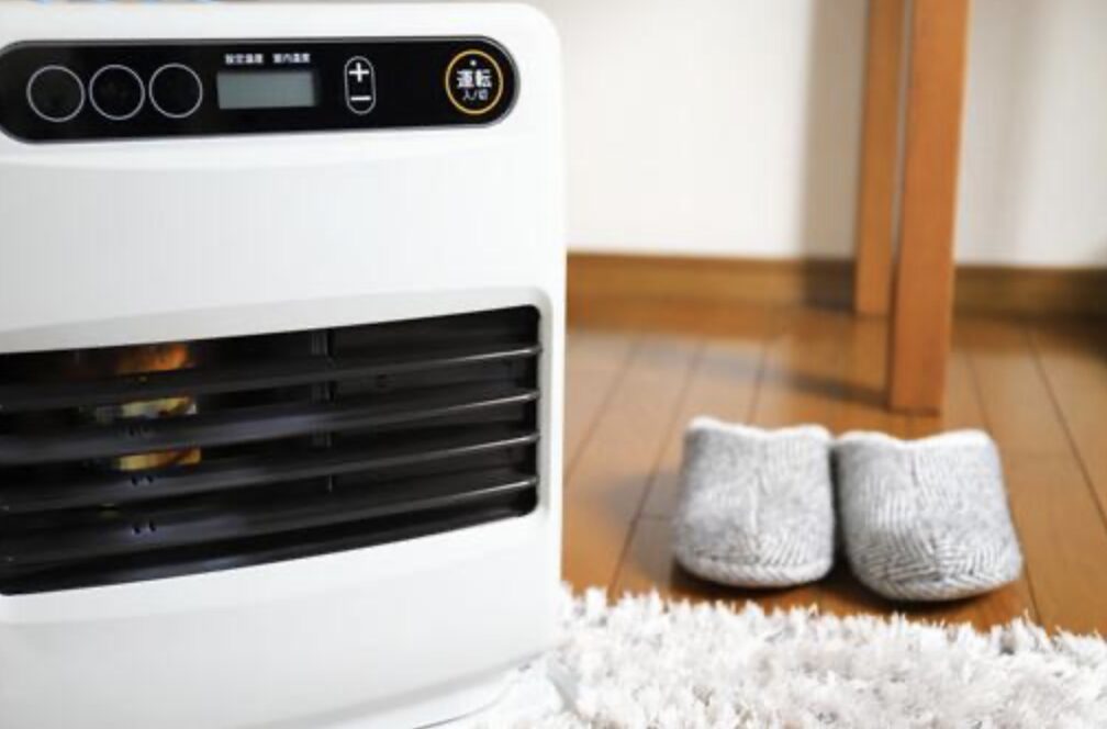 石油ファンヒーターの吹き出し口から炎が見える室内設置の様子。床に置かれたスリッパとラグが写っている。
