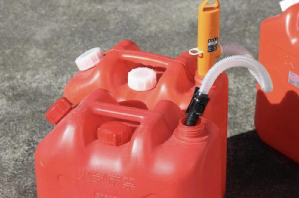 赤いポリ灯油タンクに手動ポンプを差し込み、給油準備をしている様子。屋外で使用する携行用灯油缶のクローズアップ。