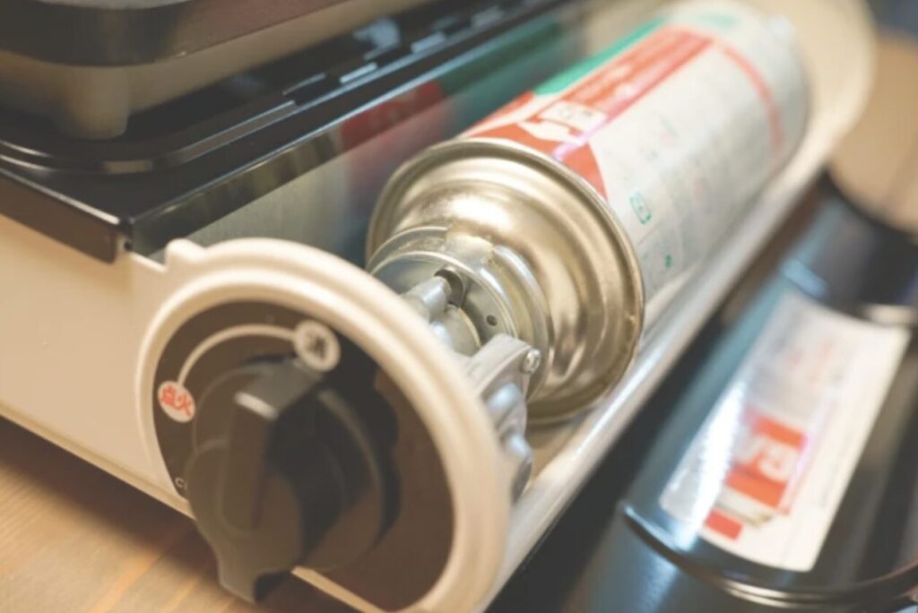 カセットコンロに正しく装着されたカセットガスボンベの接続部分。ボンベが内部に収まっている状態。