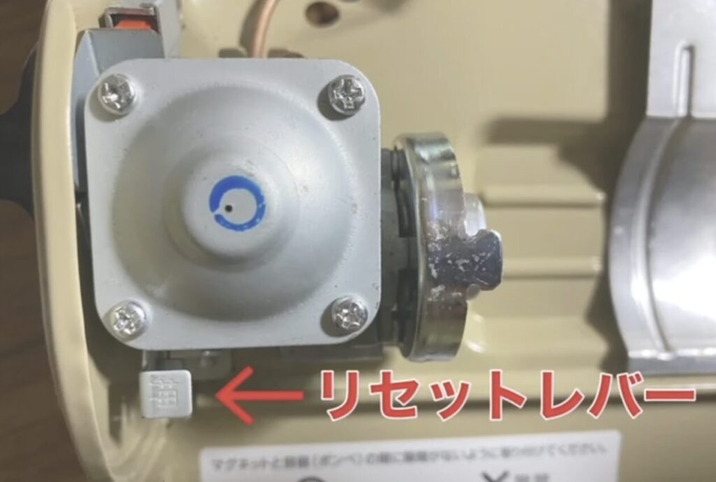 カセットコンロ内部の圧力調整部とリセットレバーの位置を示す画像。赤い矢印でレバー方向を表示。