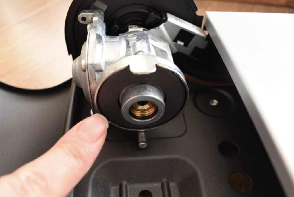 カセットコンロ内部のガス接続部を指で示している様子。ボンベ装着部の金属バルブ構造の拡大写真。