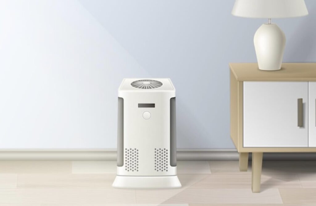 淡いブルーの壁際に設置された白い除湿機。本体上部に送風口があり、隣に木製サイドテーブルとスタンドライトが置かれている室内風景。