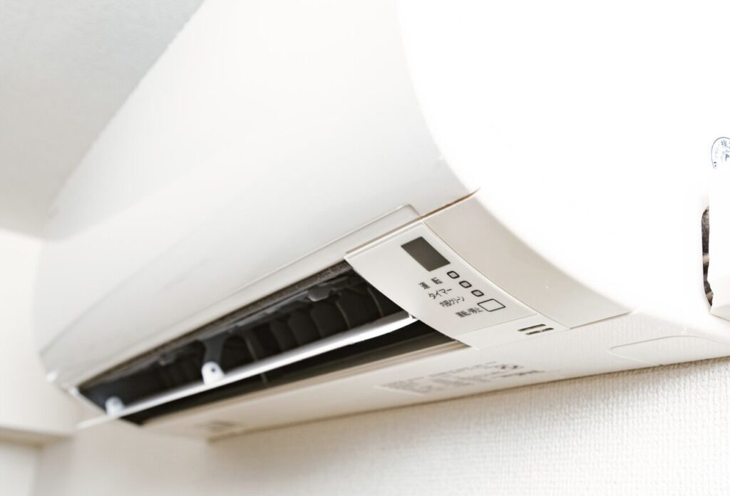 壁掛けエアコンの吹き出し口を下から撮影したクローズアップ。風向ルーバーと操作表示部が見える状態。