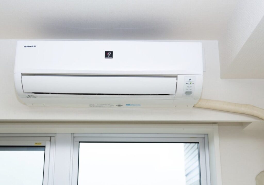 窓上に設置された壁掛けエアコン本体の正面写真。白い室内壁と配管カバーが確認できる設置状態。