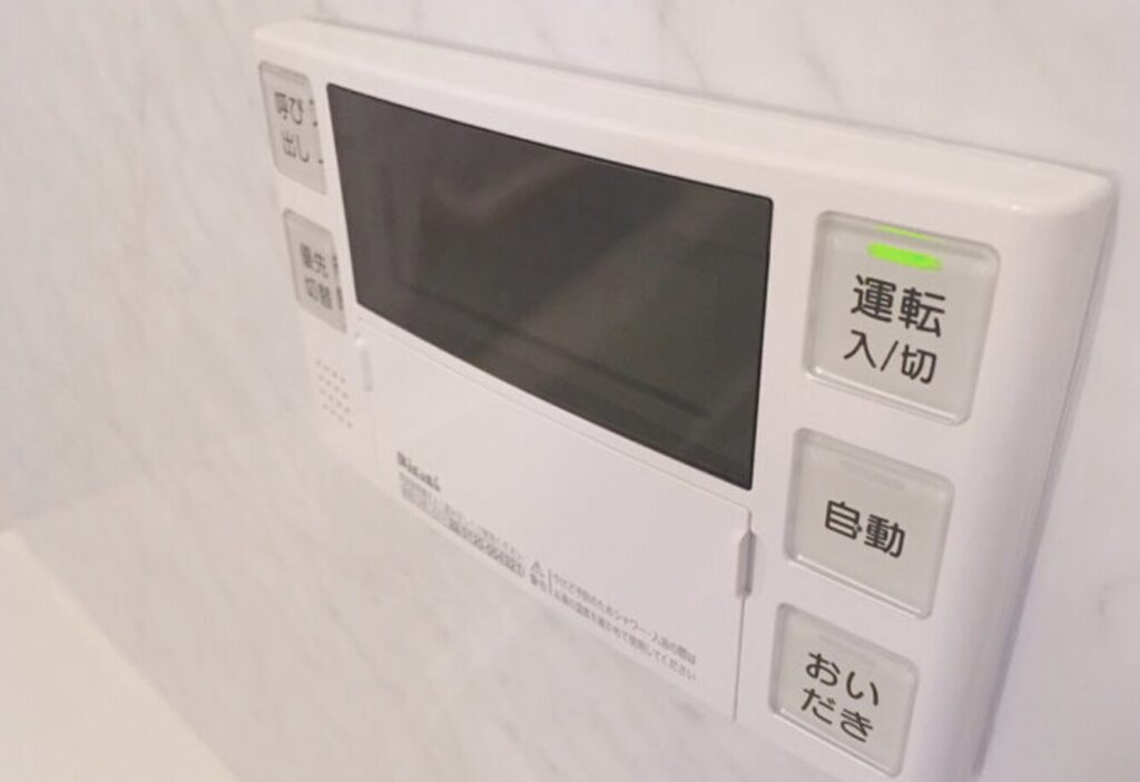 浴室壁面に設置された給湯器リモコン。「運転 入/切」「自動」「おいだき」ボタンが並ぶ操作パネル。