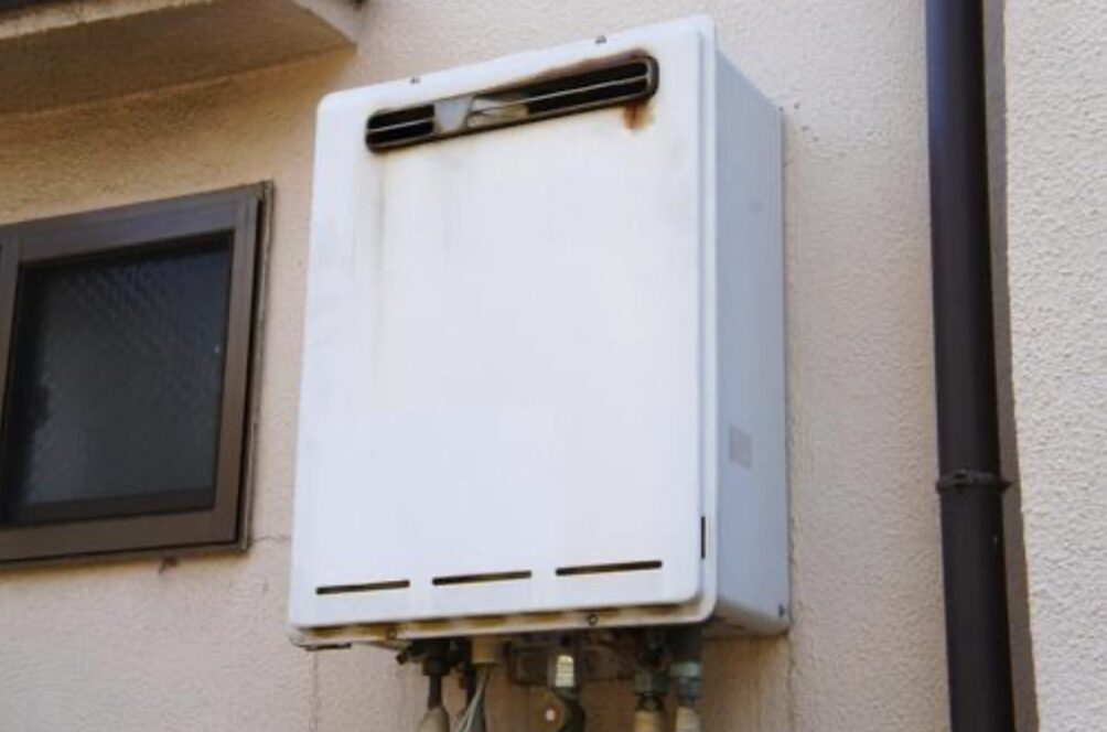 住宅の外壁に設置された壁掛け型ガス給湯器の外観。上部に排気口があり、配管が下部から接続されている設置状態。