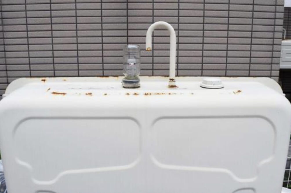 屋外設置の灯油タンク上部。軽度の錆が点在し、給油口キャップと通気管が確認できる状態