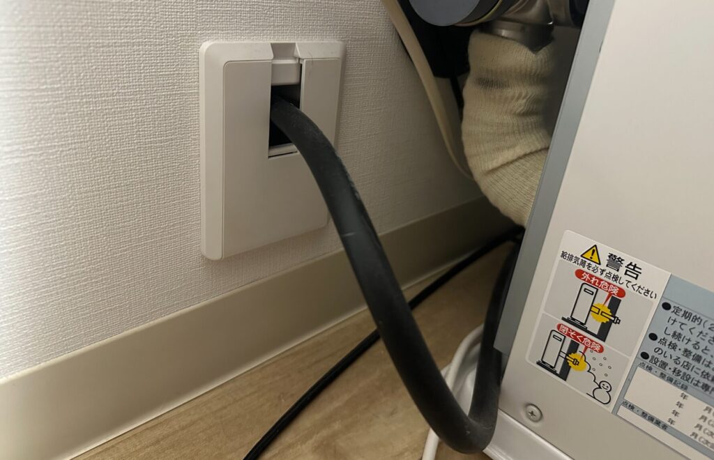 壁面の配線カバーから黒い送油ホースが通り、室内の石油ストーブ本体へ接続されている様子