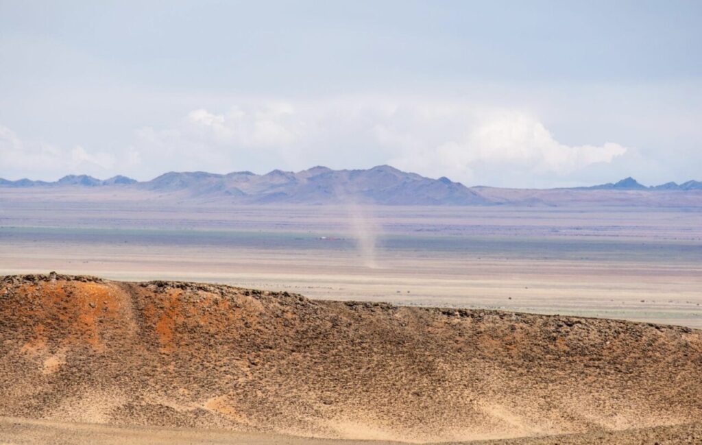 乾燥した大地に舞い上がる砂ぼこりと遠くに見える山並み