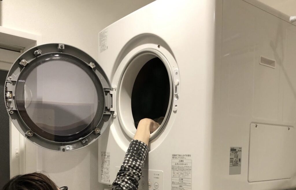 ガス衣類乾燥機のドアを開けて内部に手を入れている様子。丸型扉と内部ドラムが見えるクローズアップ。