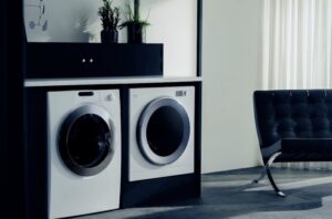 ブラックの収納棚にビルトインされた洗濯機と乾燥機。横並びに設置され、隣にレザーチェアが置かれたスタイリッシュな空間。