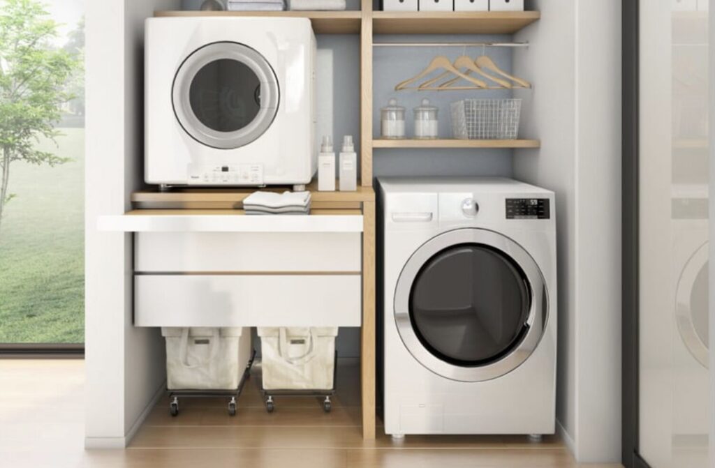 木目収納棚に設置されたガス衣類乾燥機とドラム式洗濯機。ハンガーや収納ボックスが並ぶ明るいランドリースペース。