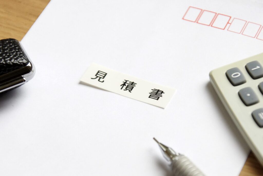 「見積書」と書かれたラベルが置かれた書類と電卓、ボールペンのクローズアップ。費用計算をイメージした写真。