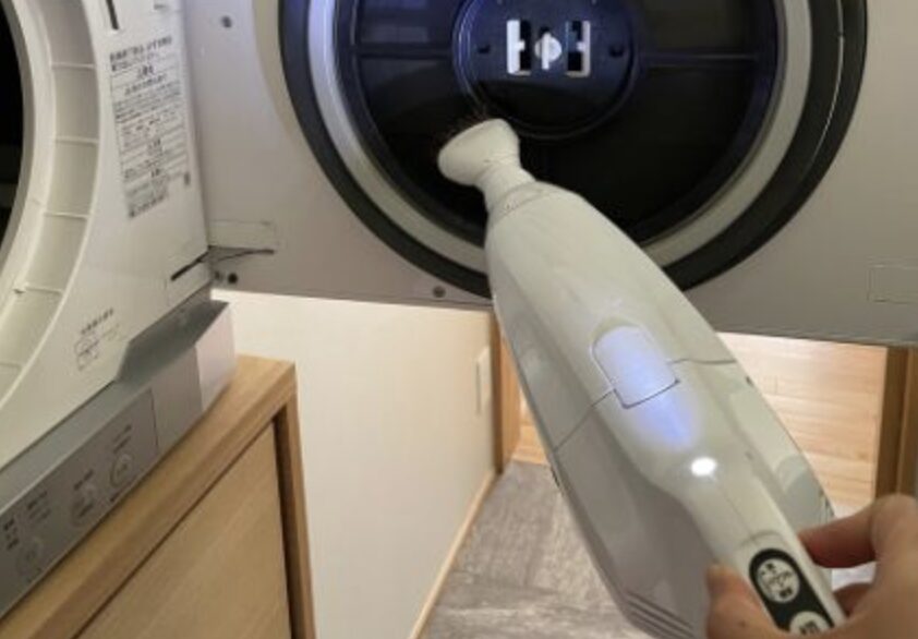 乾燥機内部にハンディクリーナーを差し込み、内部のホコリを吸い取っているメンテナンス作業の様子。