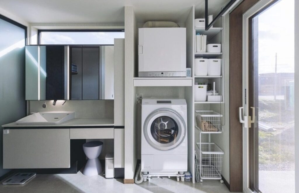 洗面台横の収納スペースに設置されたガス衣類乾燥機とドラム式洗濯機。整理されたランドリールームの全体風景。