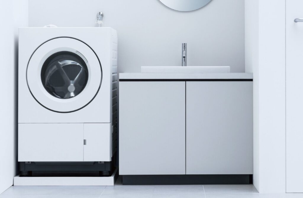 白を基調としたシンプルな洗面スペースに設置されたドラム式洗濯機と洗面台収納の様子。