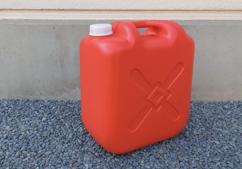 赤いポリタンクが砂利の上に置かれ、コンクリート壁を背景に撮影された灯油用容器の外観写真。