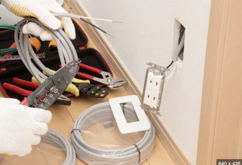壁から出た電線を工具で加工し、コンセントを取り付ける準備をしている作業中の手元。