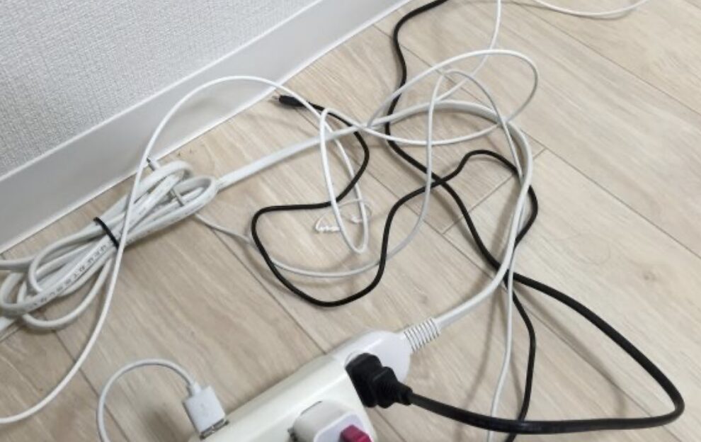 床に置かれた延長コードと絡まった配線。電源タップに複数のプラグが接続されている様子。