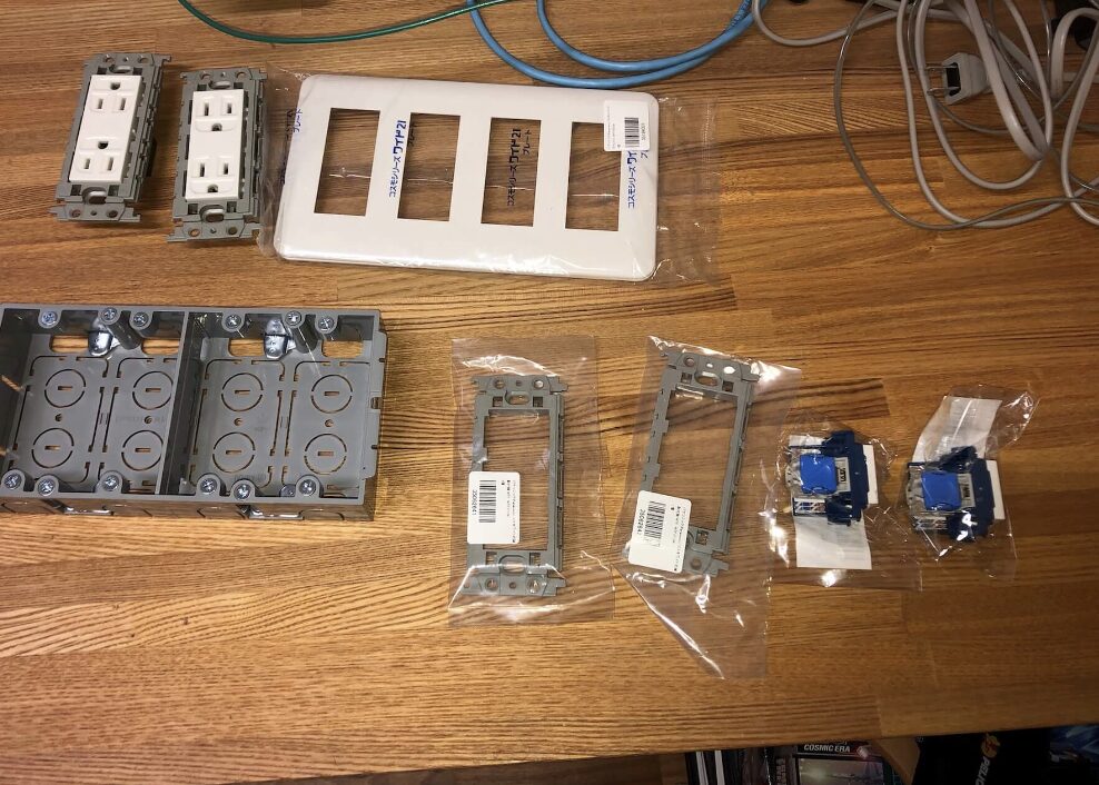交換用のコンセント本体や取付枠、プレートなどの電気部材が木製テーブルの上に並べられている状態。